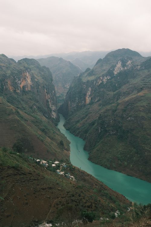 Free A breathtaking view of a turquoise river winding through a lush mountain canyon under a cloudy sky. Stock Photo