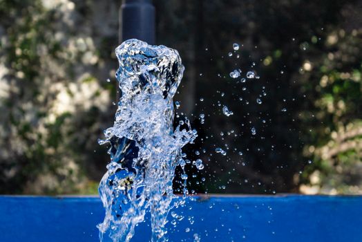Close-up of water splashing from a fountain with droplets frozen in motion against a blurred outdoor background.