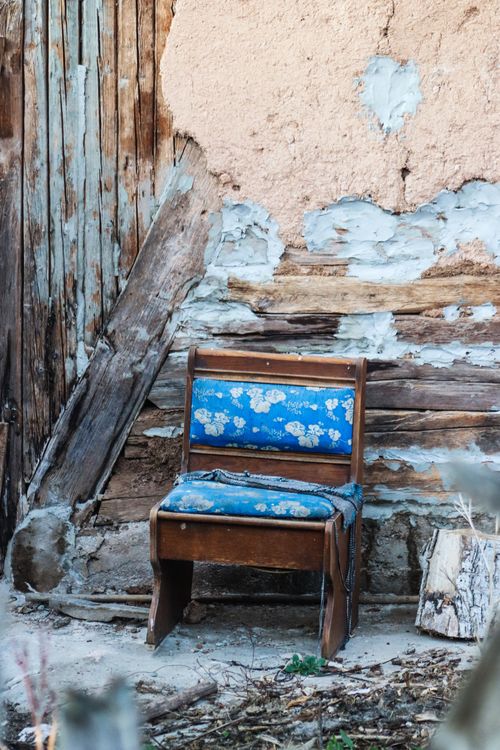 Free A vintage wooden chair with blue upholstery against a textured rustic wall, ideal for rustic decor themes. Stock Photo
