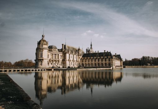 Stunning view of Château de Chantilly with reflection in a serene lake under a clear sky in France.