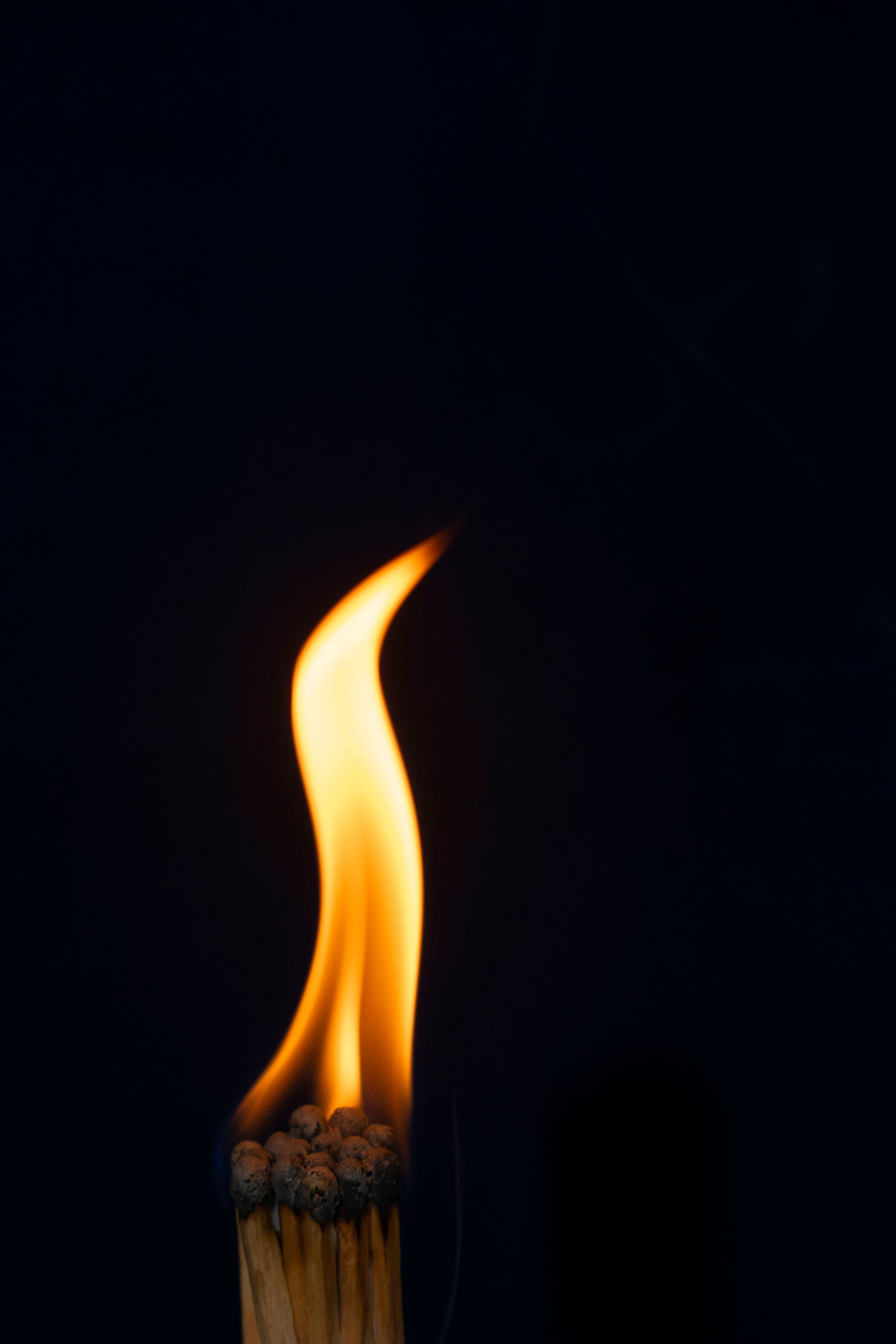 A dramatic close-up of a burning matchstick emitting a warm glow against a black backdrop.