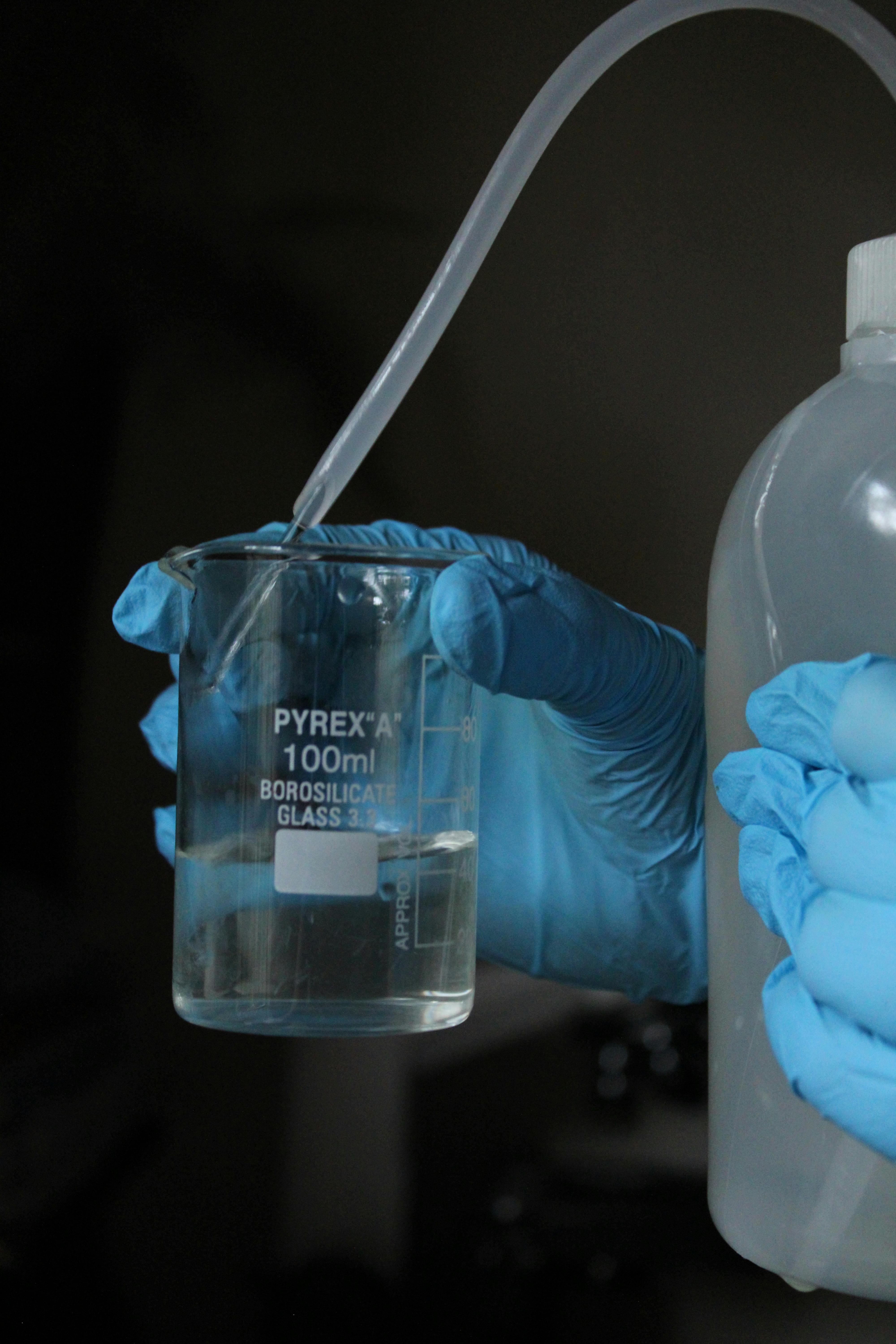 A laboratory setup with liquid in a Pyrex beaker and gloved hands.