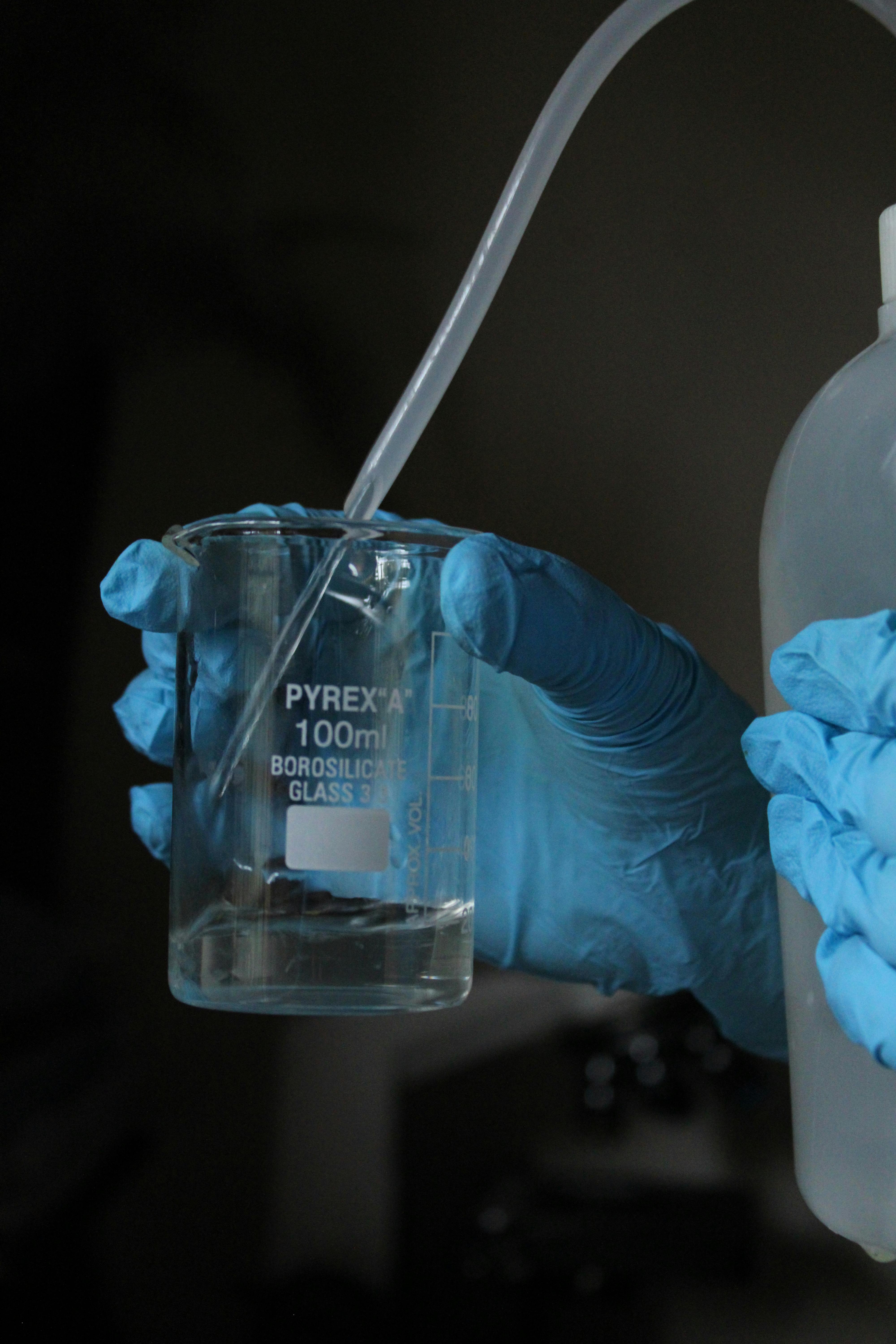 Lab technician pouring liquid into a Pyrex beaker with precision and care.