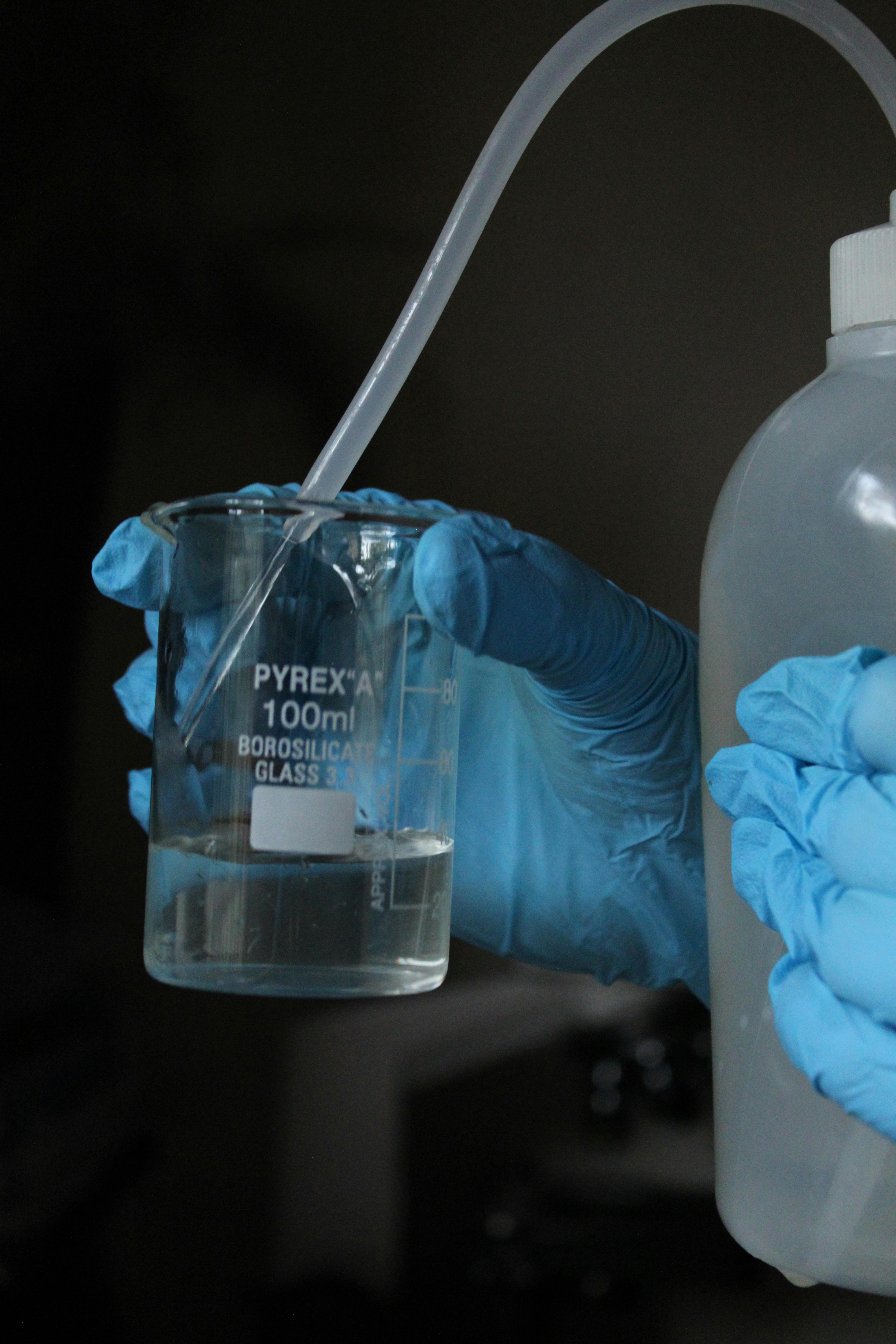 Close-up of gloved hands holding beaker and bottle, showcasing laboratory equipment.