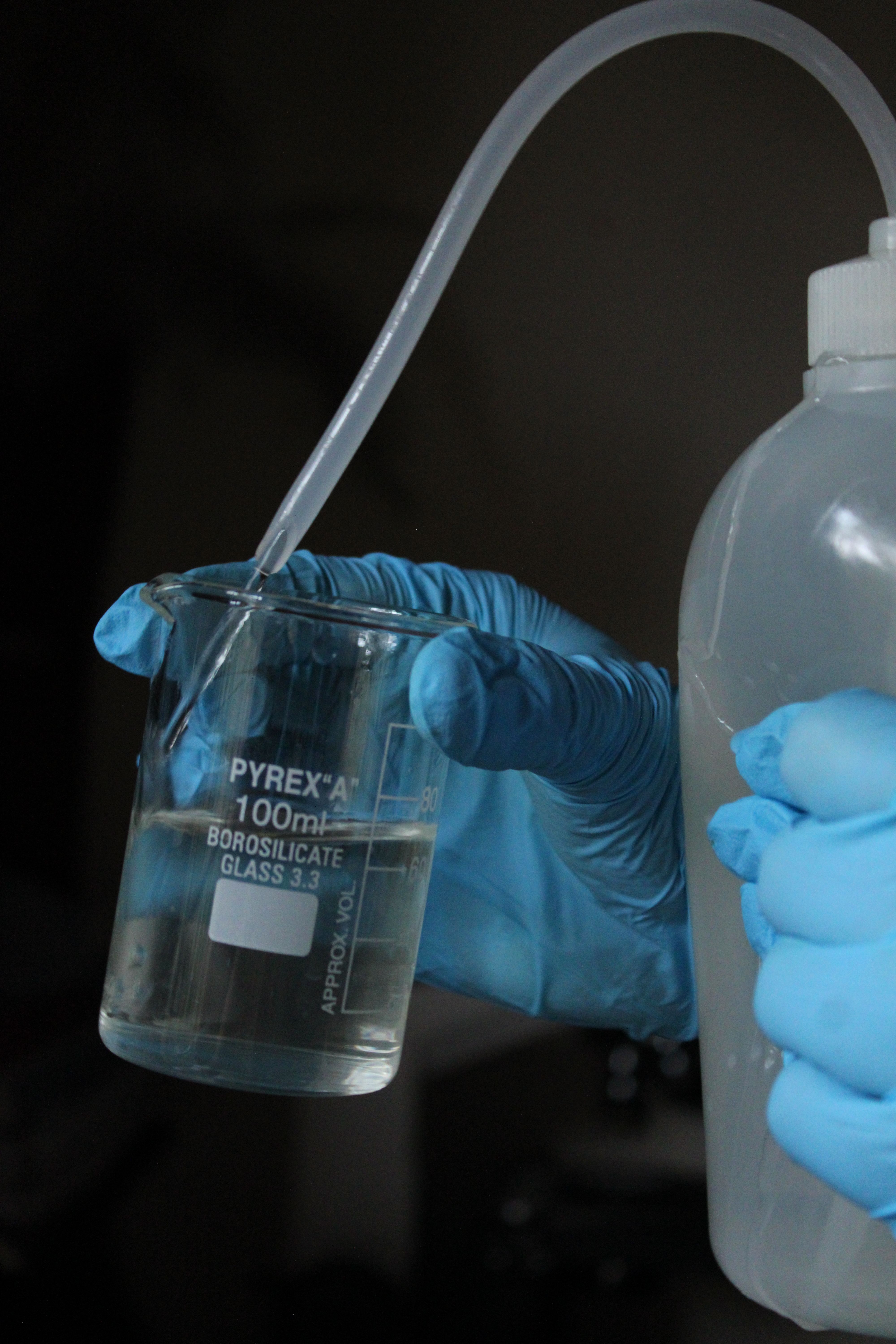 Scientist wearing gloves conducting a liquid experiment using a Pyrex beaker.