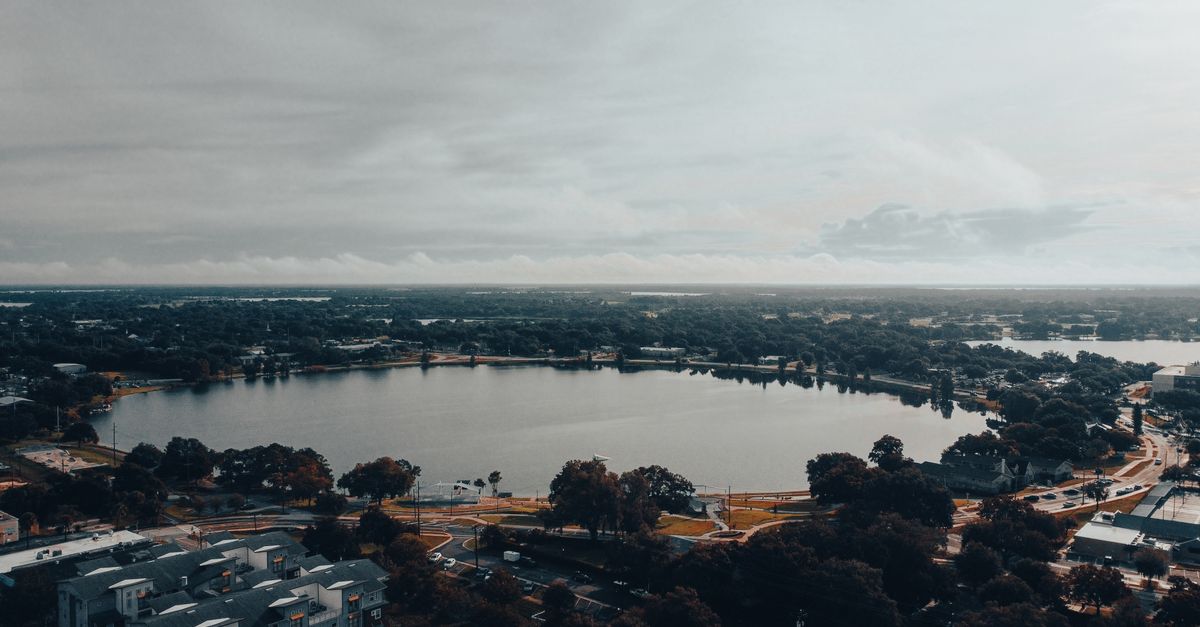 A stunning aerial view capturing a serene urban lake surrounded by cityscape and lush greenery.