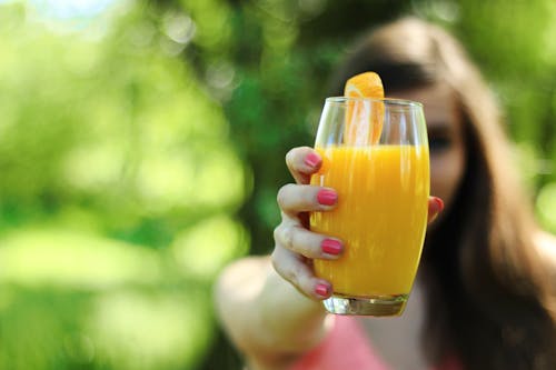 Woman in Pink Top Holding Orange Juice in Glass Cupo