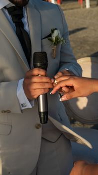 Close-up of a groom placing a ring on the bride's finger during an outdoor wedding ceremony.