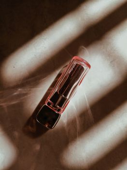 A close-up of a lipstick tube displaying dramatic shadows and light on a textured surface.
