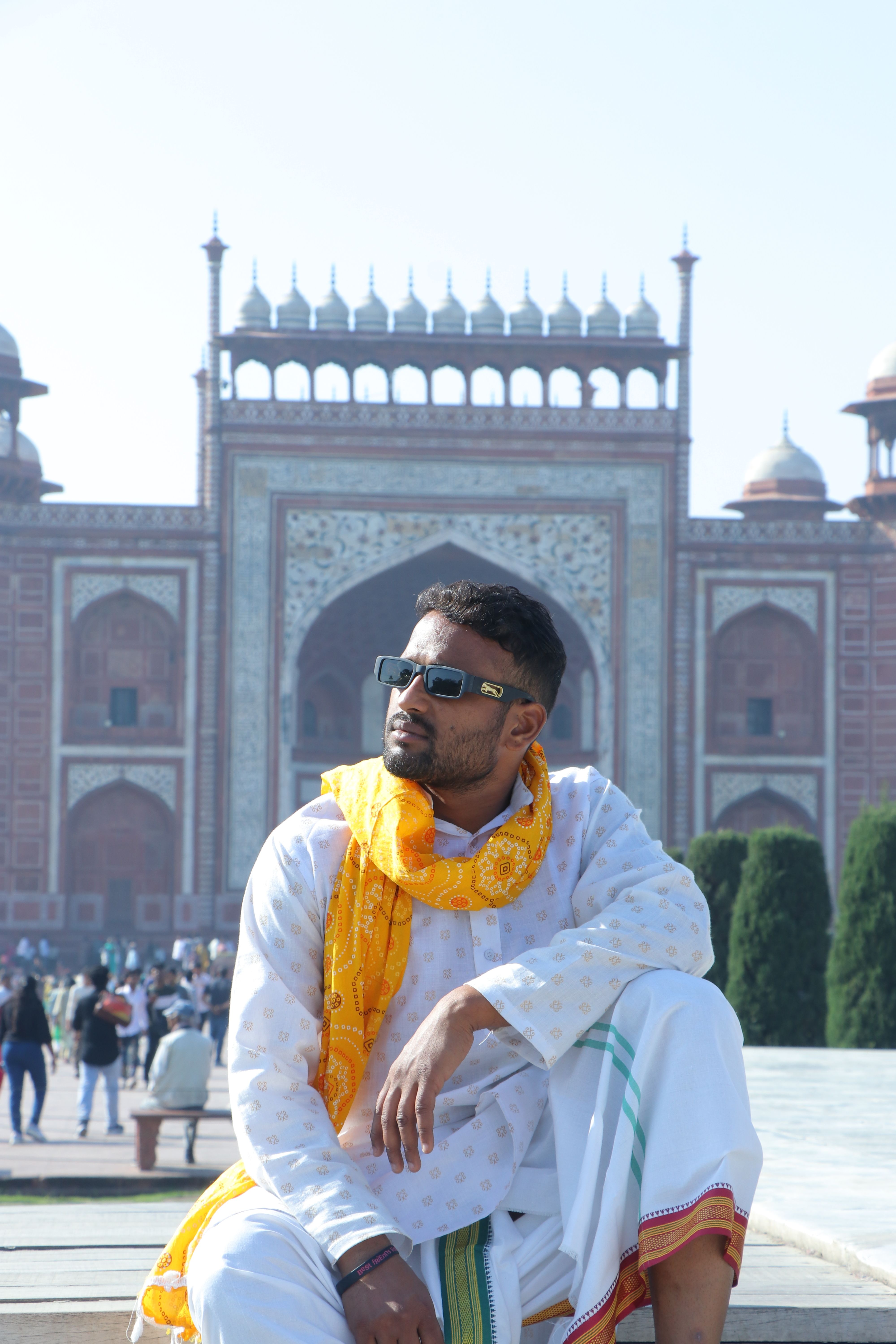 Man in vibrant Indian clothing sitting in front of the Taj Mahal entrance on a sunny day.