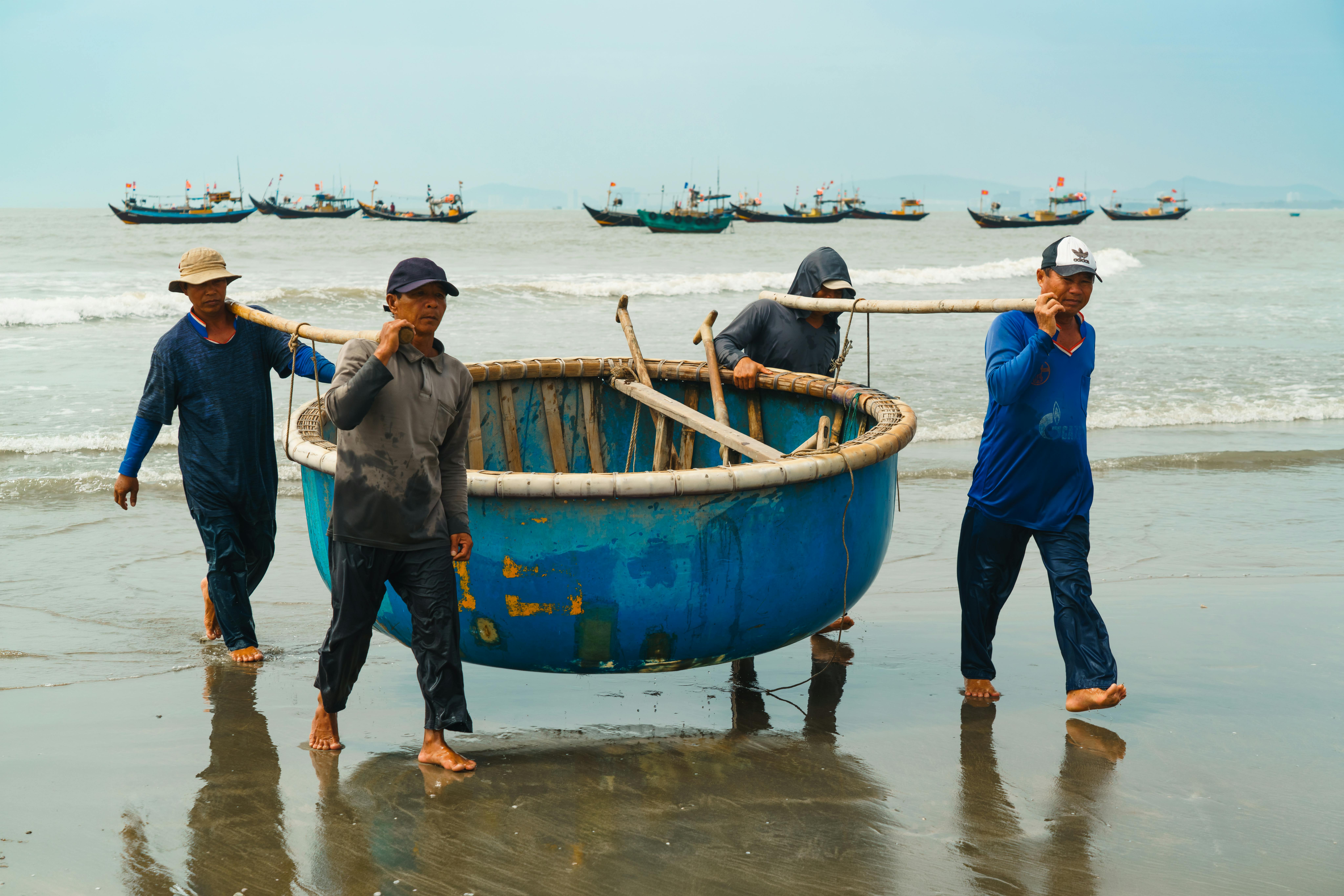 A group of Vietnamese fishermen carrying a traditional basket boat on Vung Tau beach, Vietnam.
