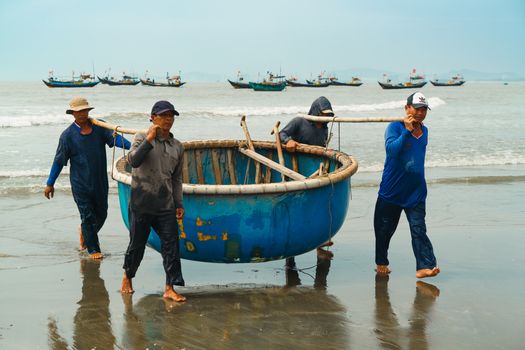 A group of Vietnamese fishermen carrying a traditional basket boat on Vung Tau beach, Vietnam.
