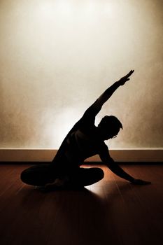 Silhouette of a person performing a yoga pose indoors with dramatic lighting.