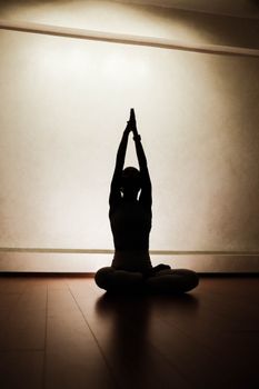Silhouette of an individual performing a yoga pose indoors, creating a serene atmosphere.