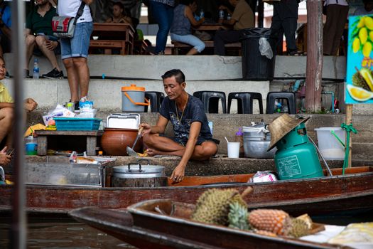 A vendor prepares food amid bustling floating market in Asia, showcasing vivid local culture.