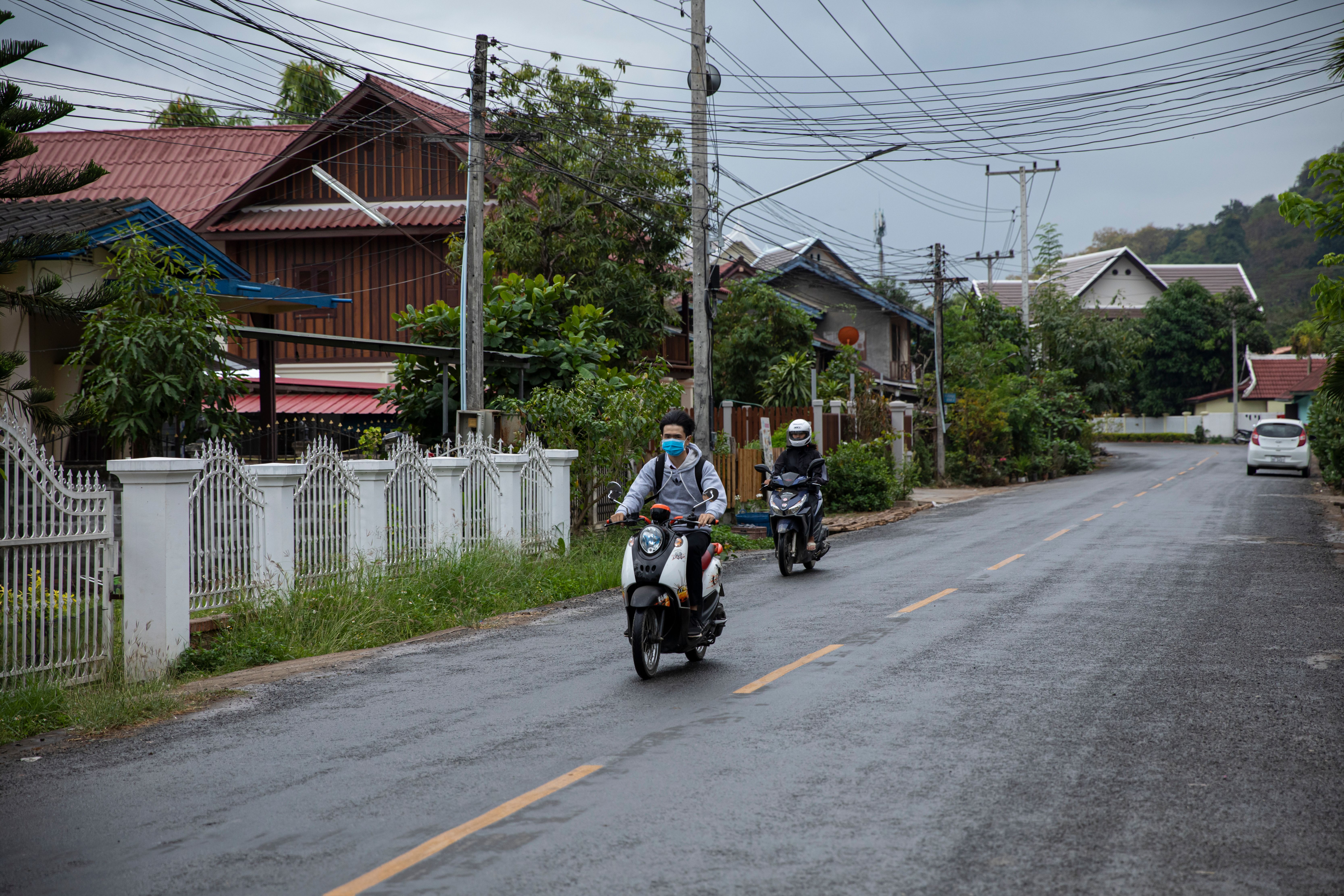 Two motorcyclists riding through a suburban street on an overcast day, highlighting daily life.