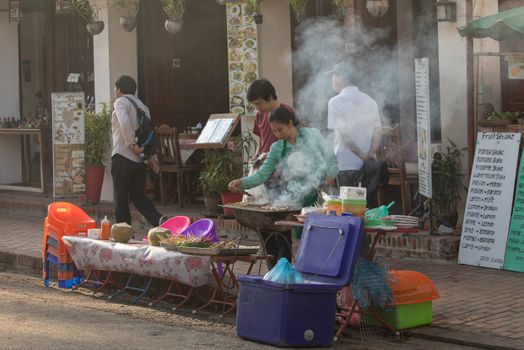 A lively scene of a street vendor preparing food at an outdoor market in daylight.