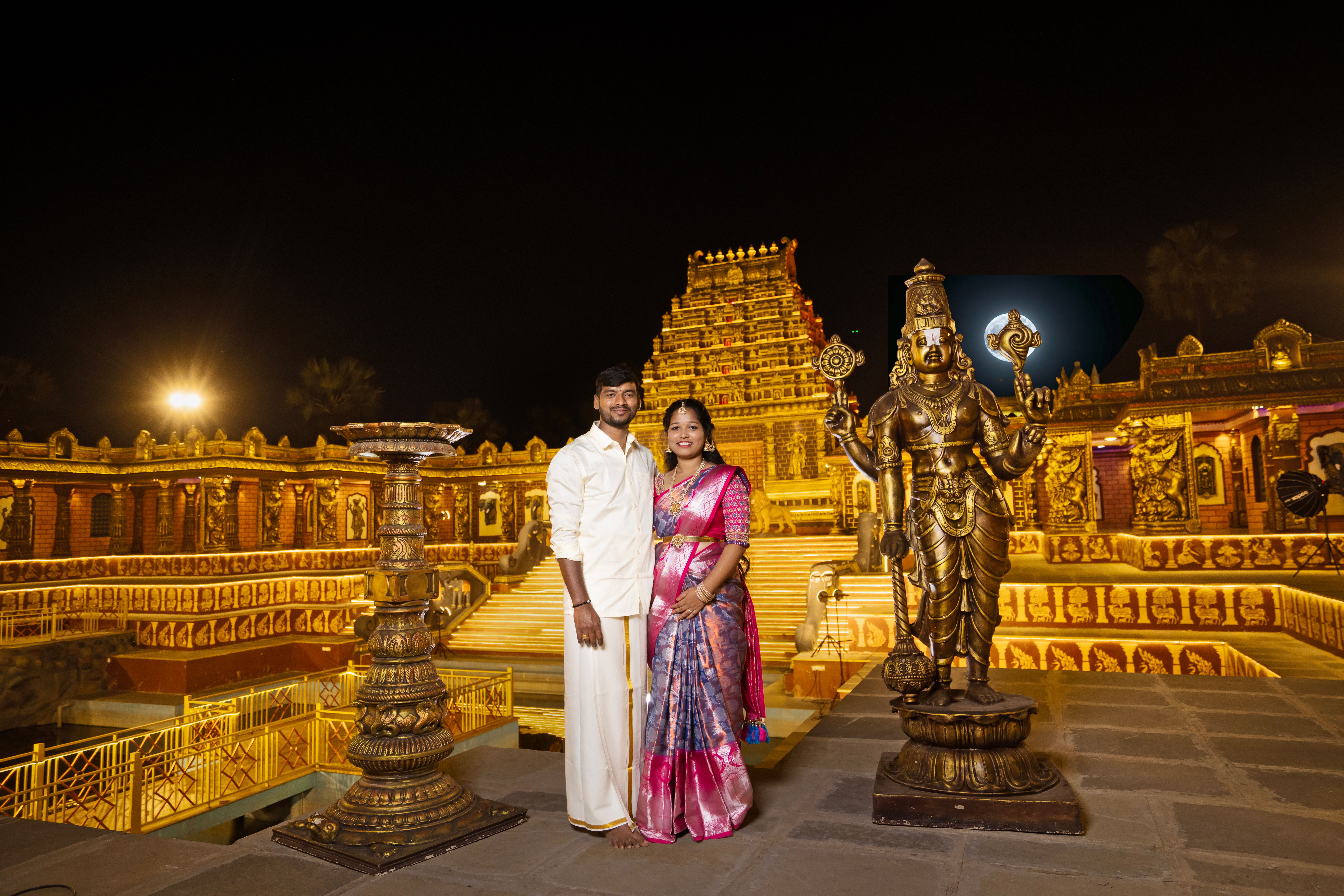 Beautiful Indian couple posing at a temple with golden lighting at night, showcasing vibrant traditional attire.