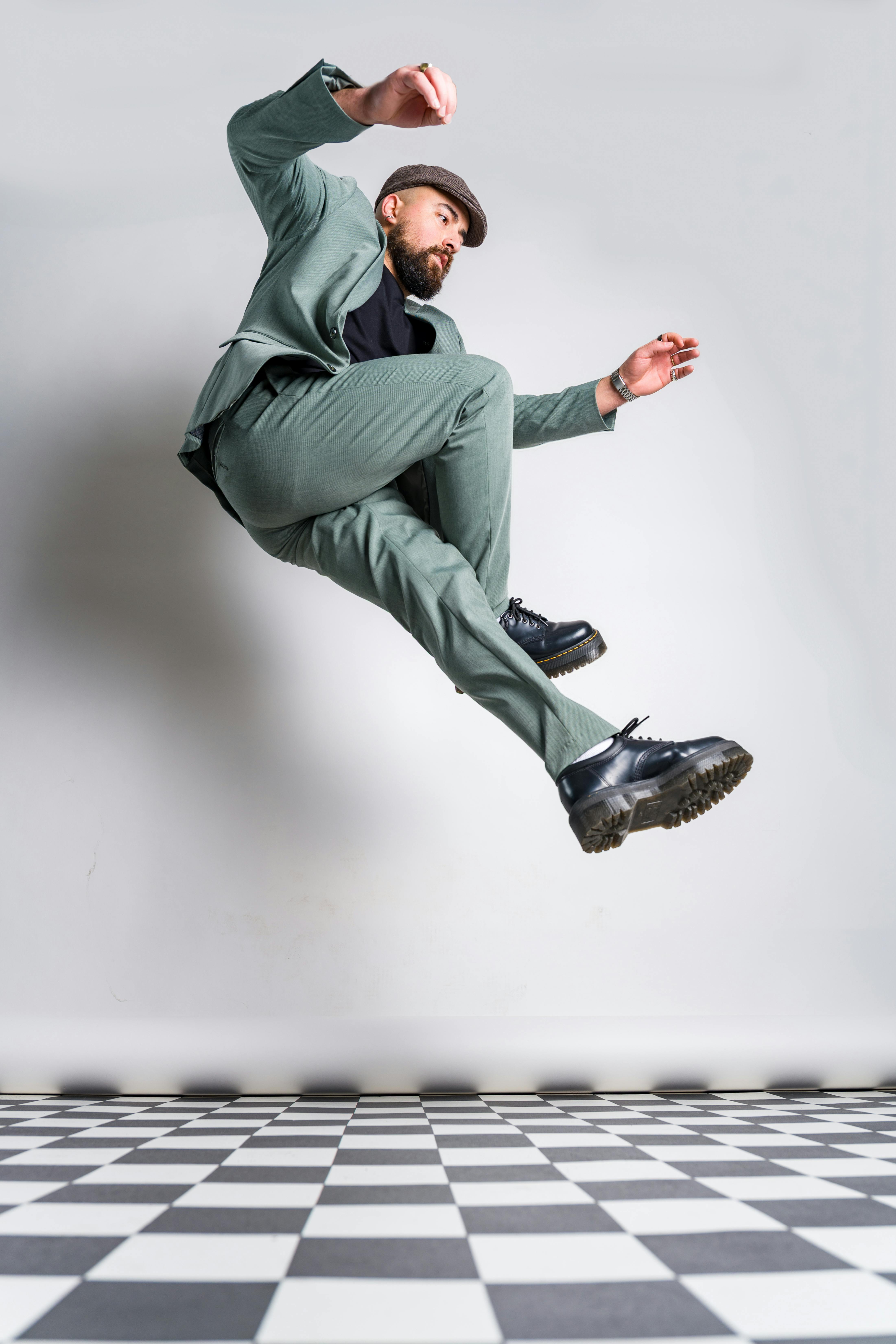 A man in a green suit and hat jumps energetically against a checkerboard floor.