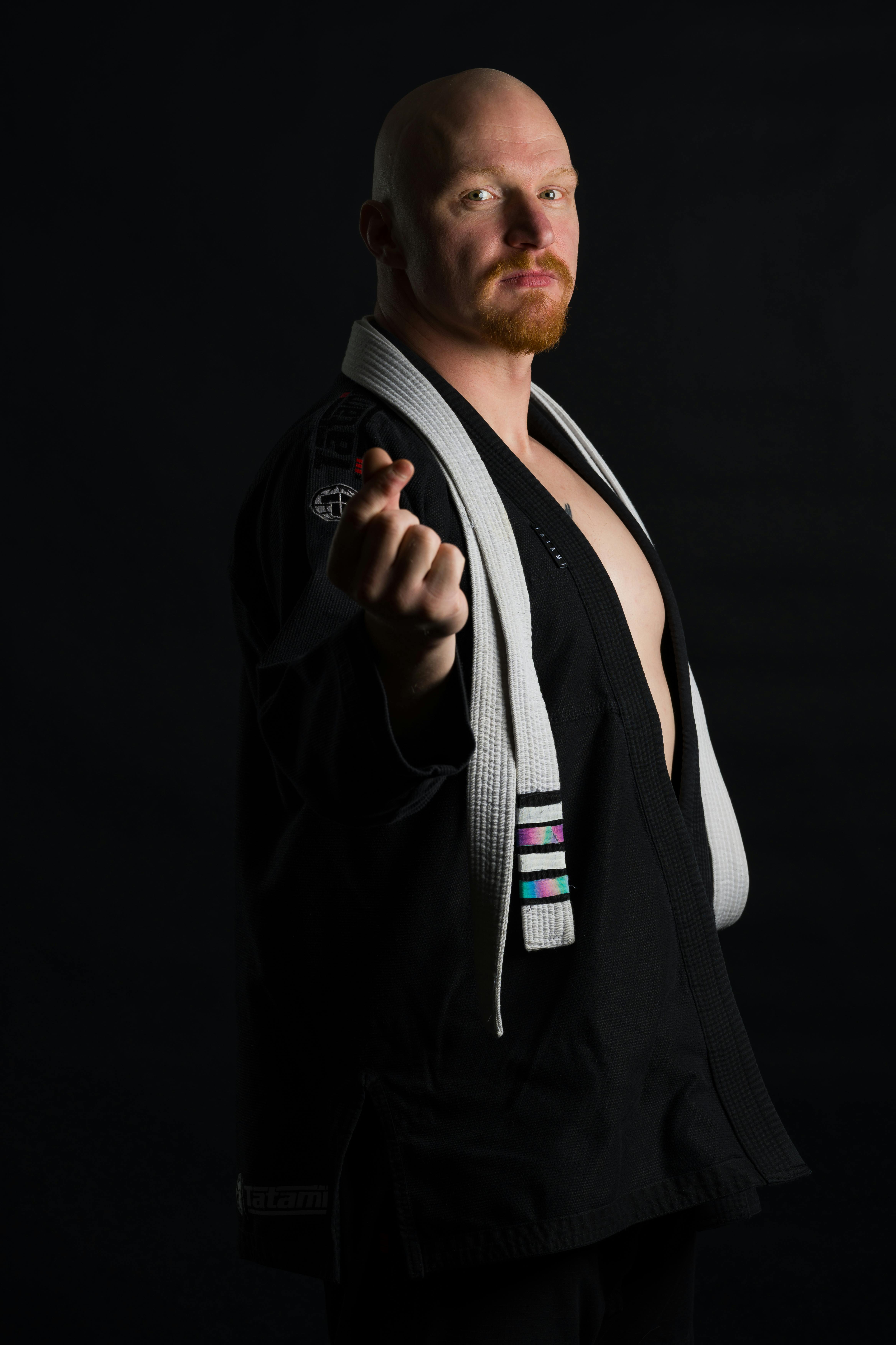 Martial artist in black gi confidently posing against dark background.