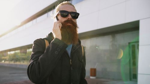 Free Casual bearded man wearing sunglasses talking on phone in urban setting. Stock Photo