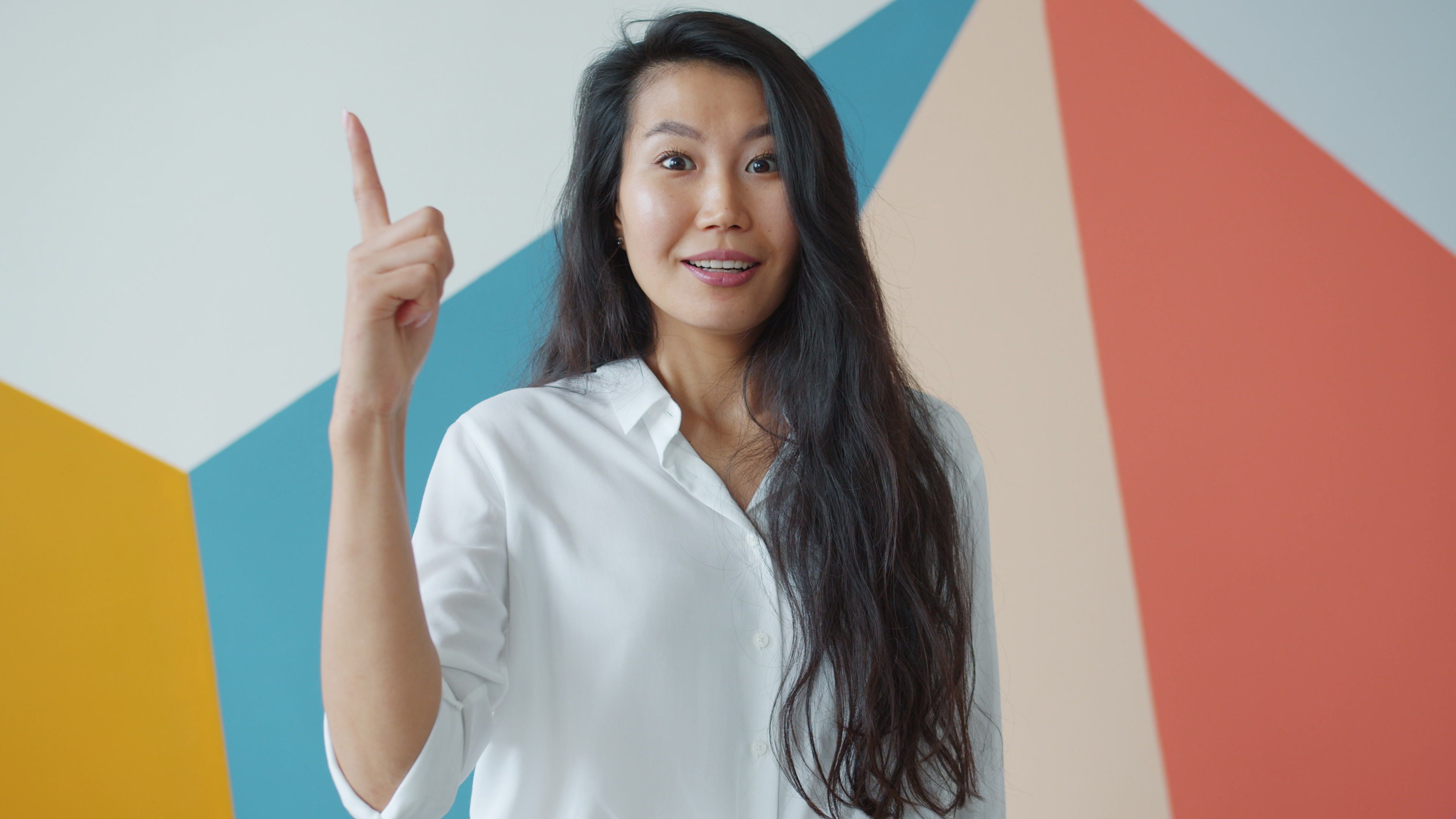 Happy woman in white shirt smiling and gesturing indoors with colorful background.