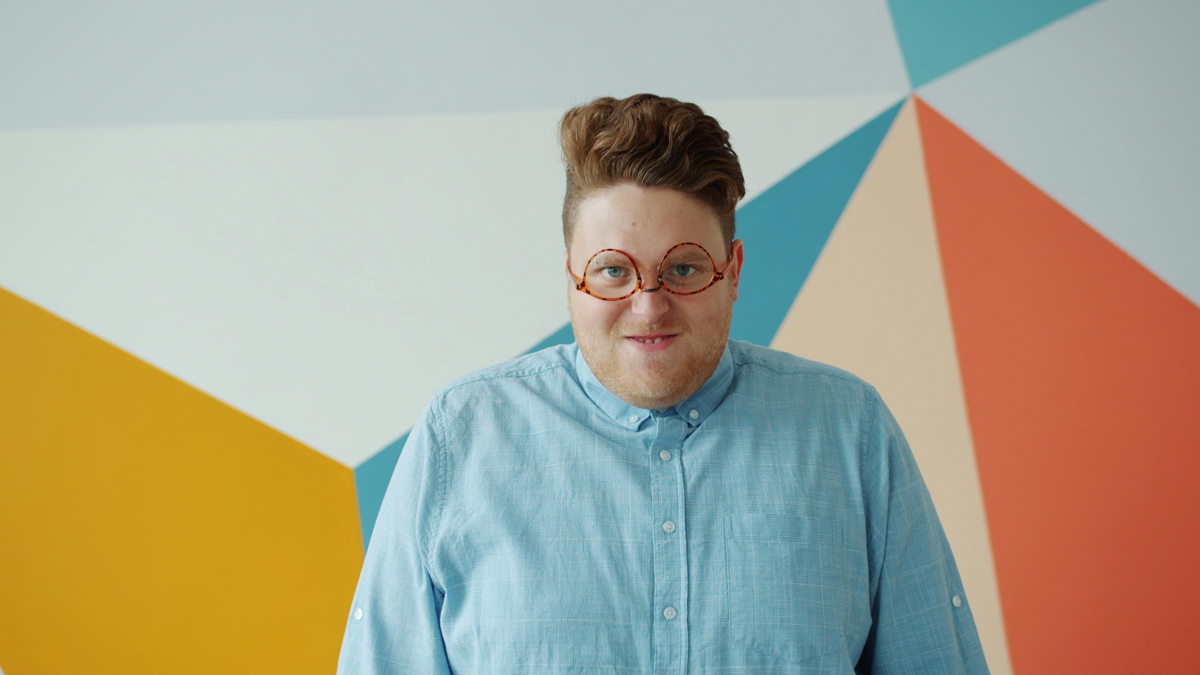 Person smiling in front of colorful geometric background wearing round glasses.