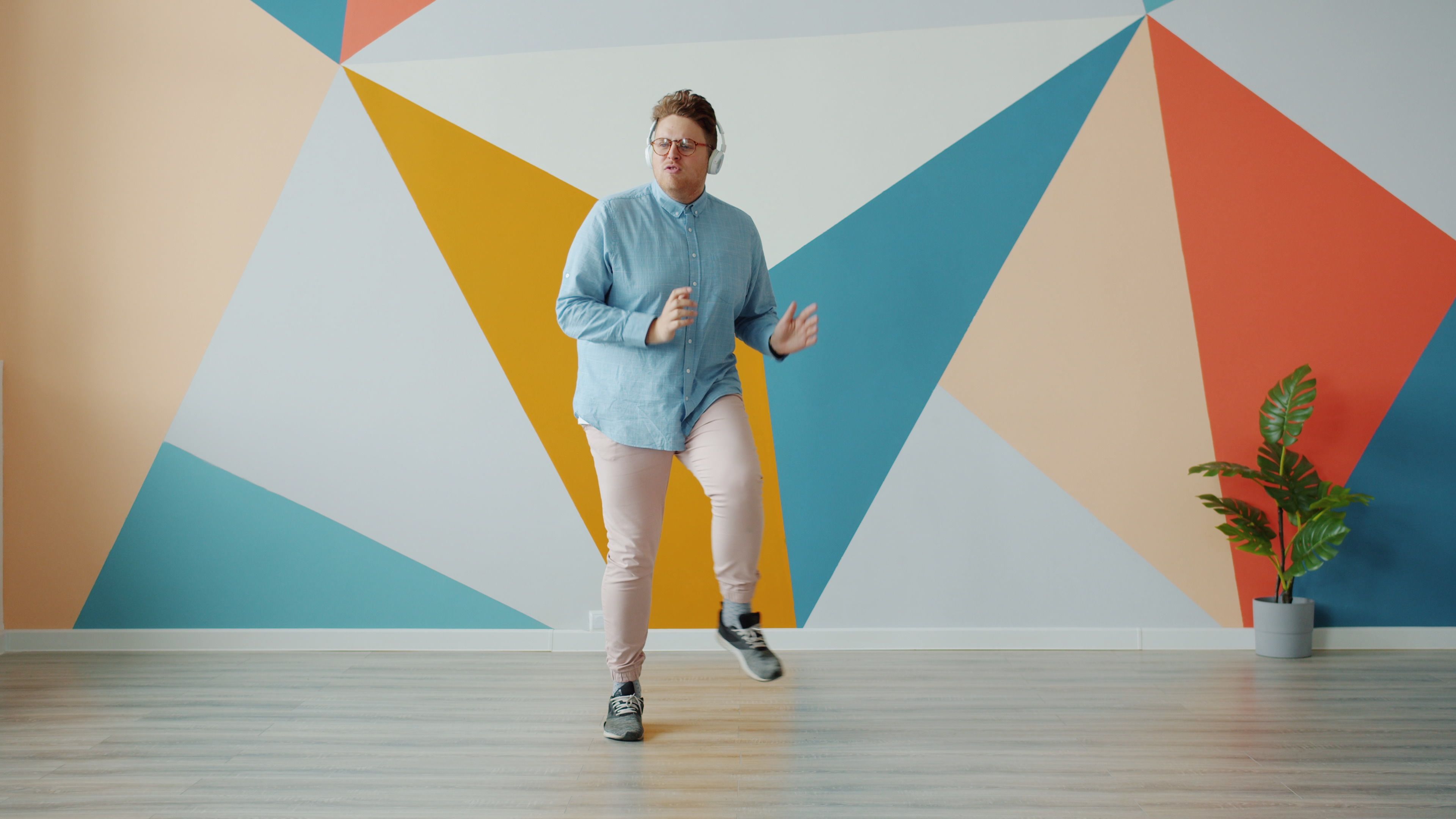 A young man dancing enthusiastically in a modern room with geometric wall design.