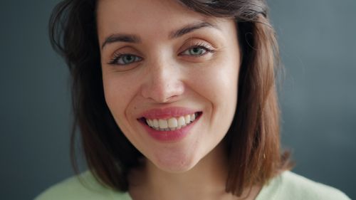 Free A close-up portrait of a smiling woman with green eyes and brown hair against a neutral background. Stock Photo