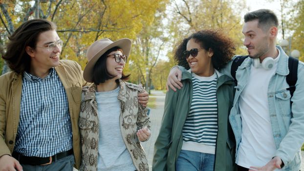 Four friends strolling in a sunny autumn park, enjoying leisure time.