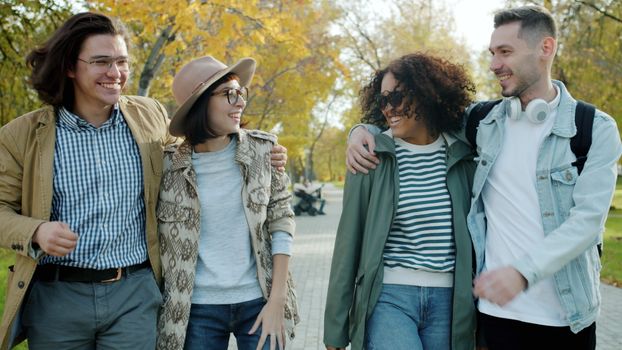 Group of friends laughing and walking in a park on an autumn day.