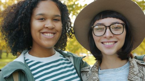 Free Two friends smiling joyfully in a sunny autumn park setting. Stock Photo