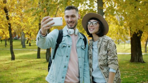 Free Happy couple taking a selfie in a vibrant autumn park, capturing the season's beauty. Stock Photo