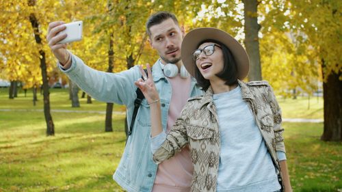 Free Young couple enjoying a fun selfie moment in a vibrant autumn park setting. Stock Photo