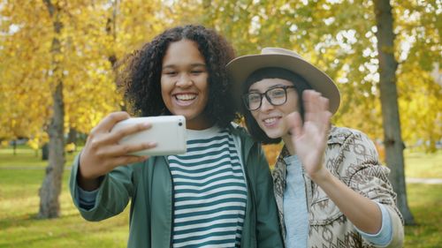 Free Two friends enjoy autumn by taking a cheerful selfie in a vibrant park. Stock Photo