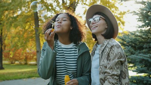 Free Two friends blowing bubbles in a sunny autumn park, enjoying leisure time. Stock Photo