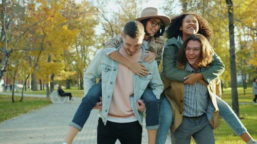 Free Group of young adults having fun with piggyback rides in a sunny park, highlighting friendship. Stock Photo