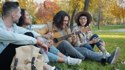 Free Group of young friends playing guitar and relaxing in a park during autumn. Stock Photo
