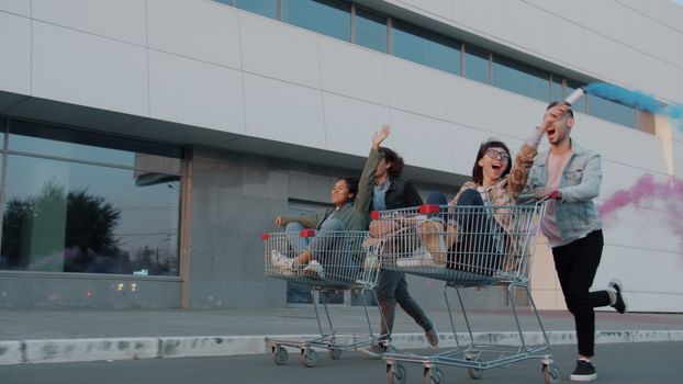 Group of friends enjoying a playful ride in shopping carts outside a building.