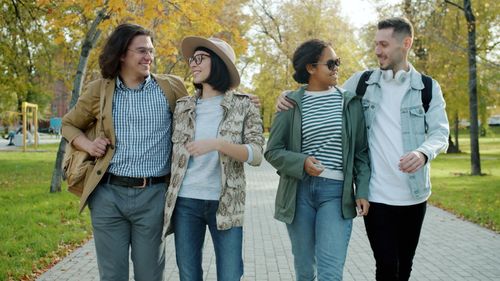 Free Four friends strolling in a sunny park with autumn leaves, smiling and engaged. Stock Photo