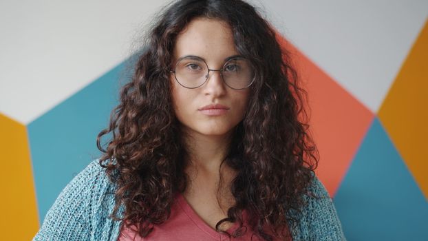 Portrait of a woman with curly hair and glasses against a colorful geometric background.