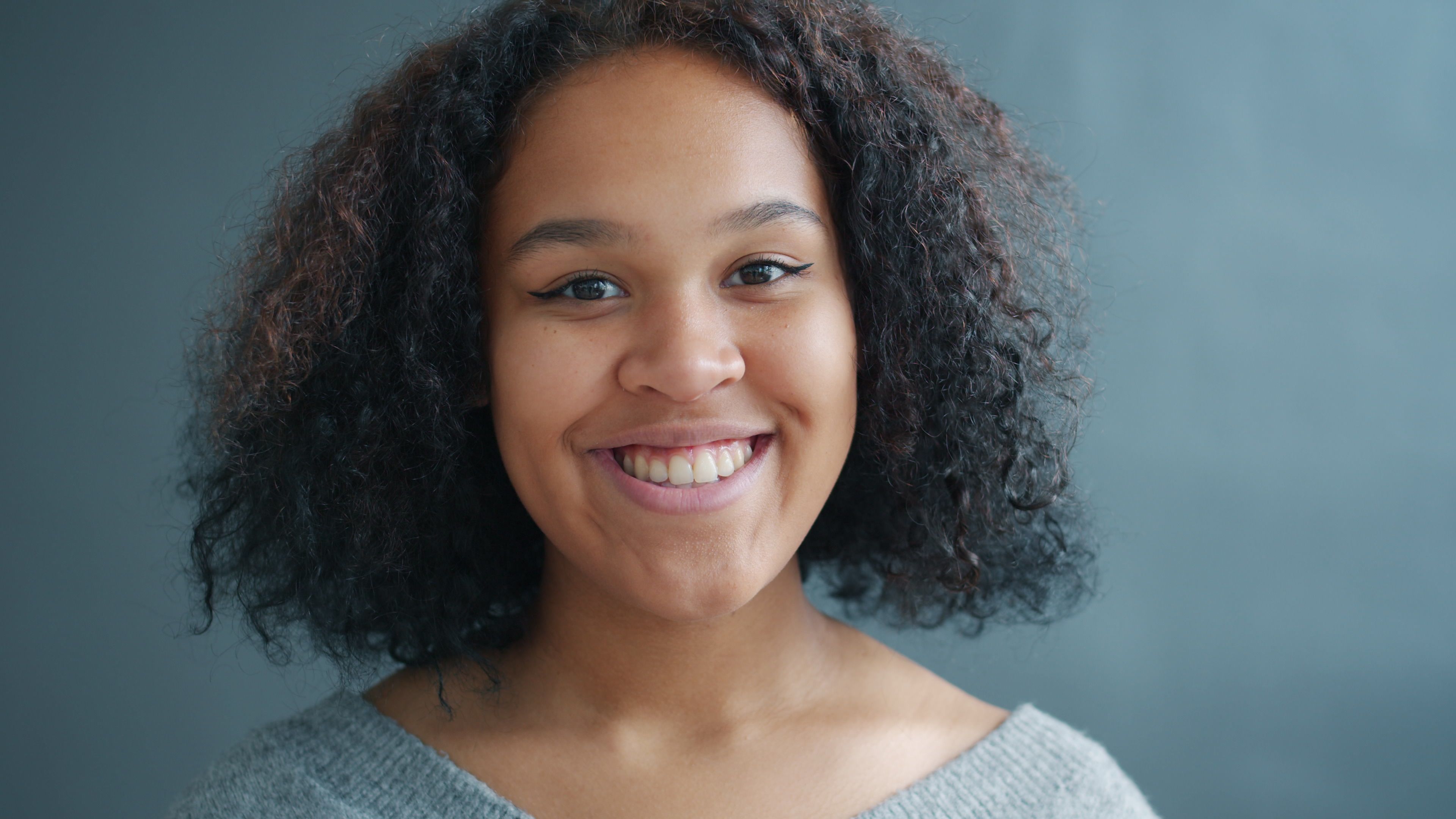Close-up portrait of a smiling woman with curly hair against a blue background indoors.