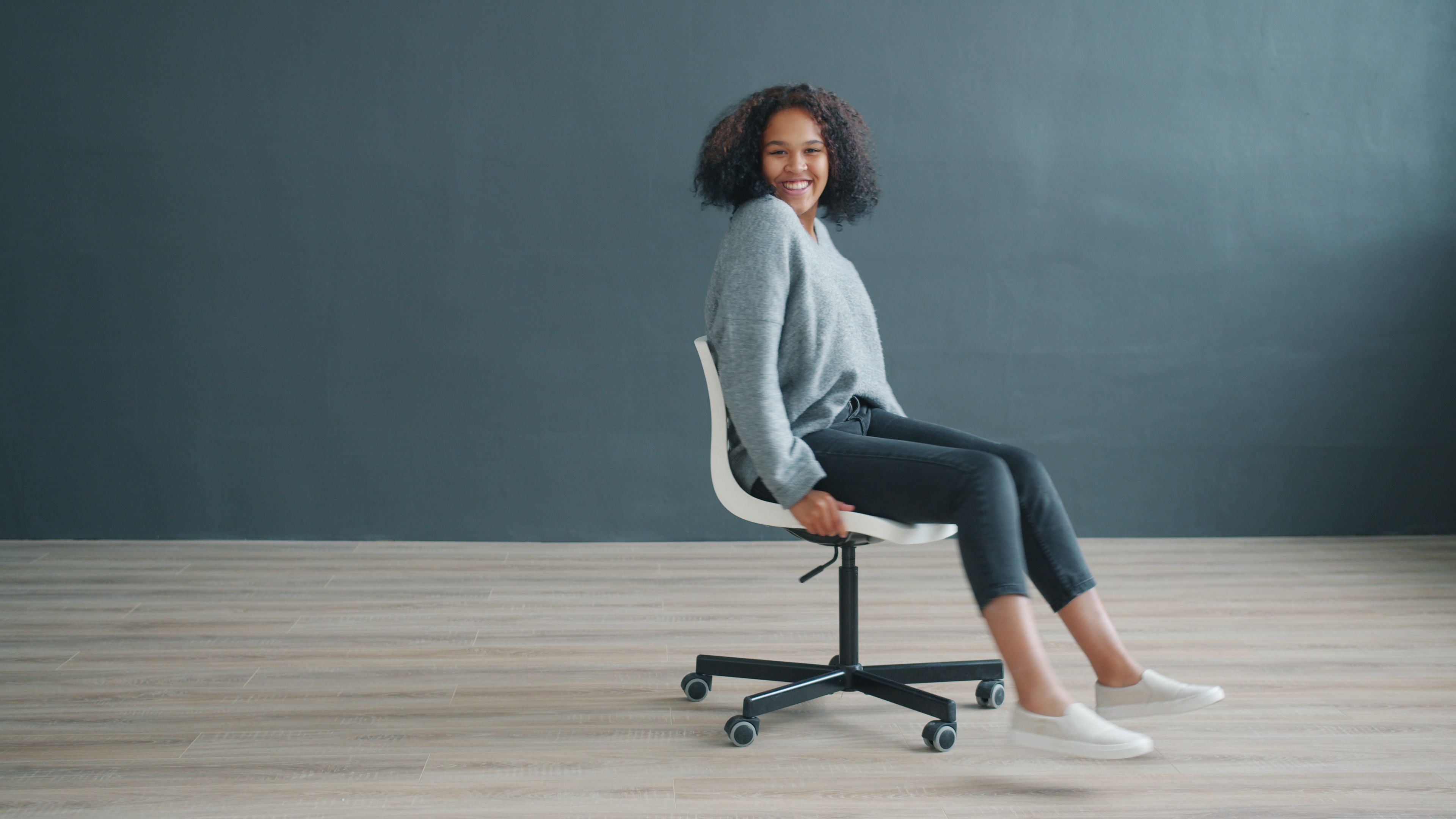 Cheerful woman spins on a chair in a minimalist room, radiating happiness.