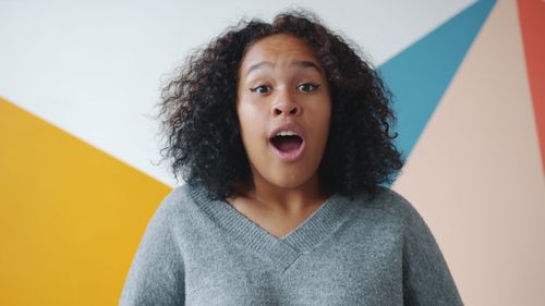 Free A young woman expressing surprise against a vibrant geometric background. Stock Photo