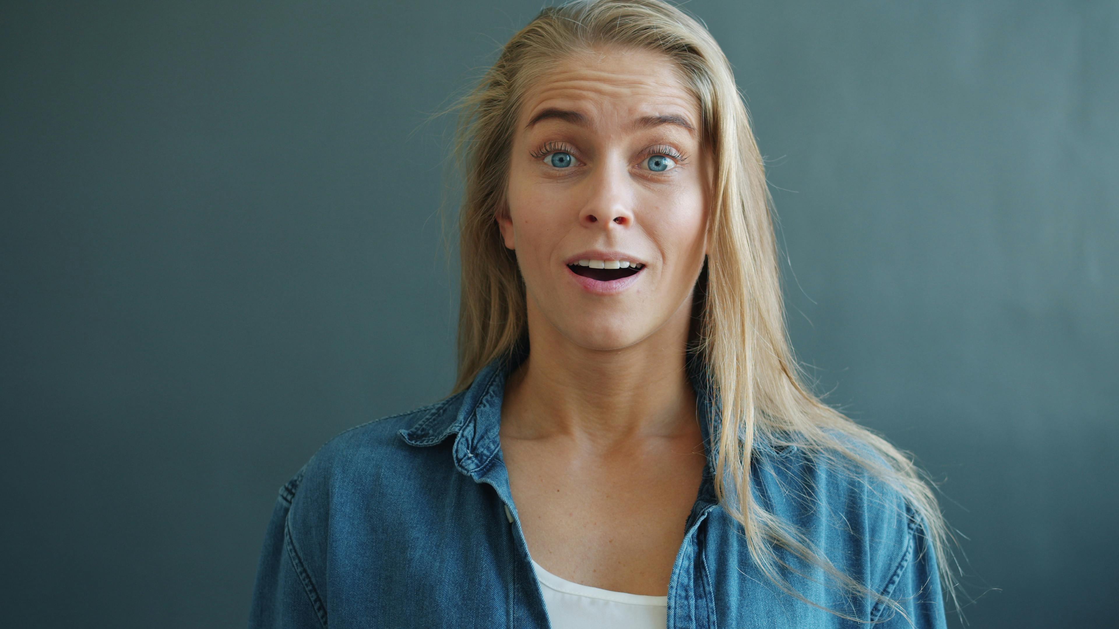 Portrait of a young woman expressing surprise against a neutral background.