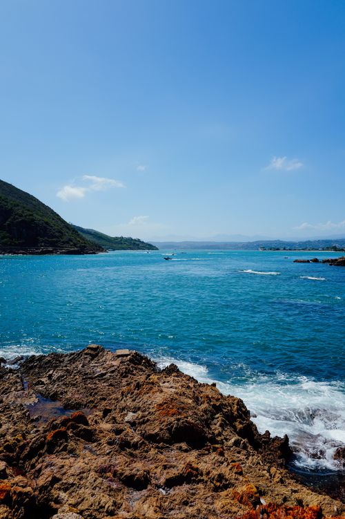 Free Beautiful coastal scene featuring clear blue waters and rocky shore under a bright sky. Stock Photo