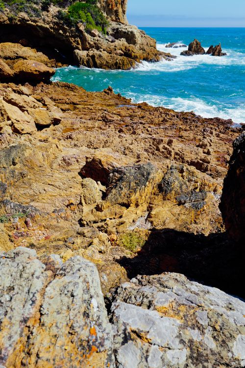 Free A scenic view of rugged coastal rocks by the ocean under a bright blue sky. Stock Photo