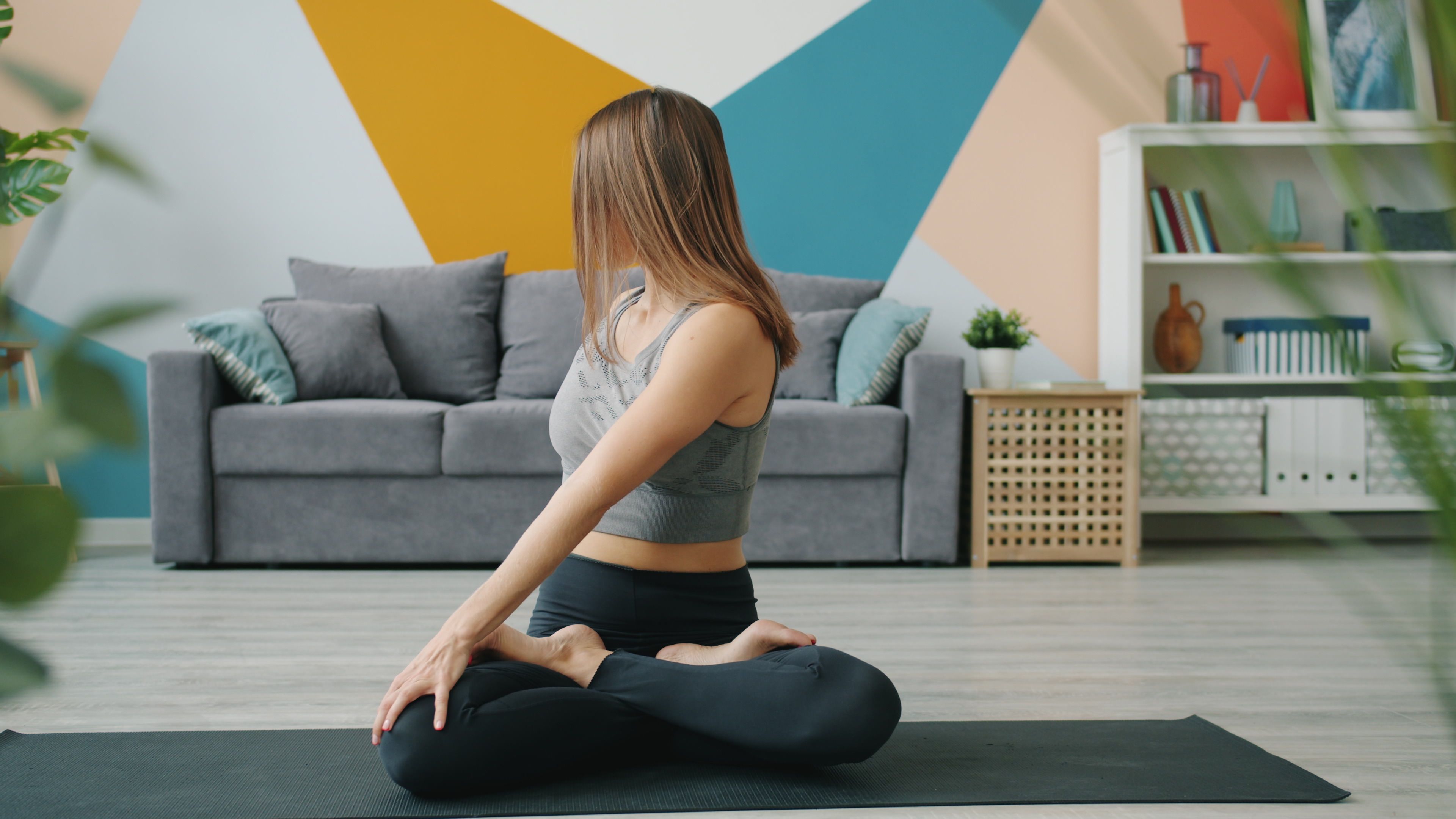 A woman doing yoga indoors on a mat in a modern living room setting.