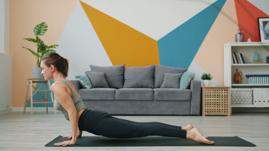 Woman practicing yoga at home in a modern living room with geometric wall art.