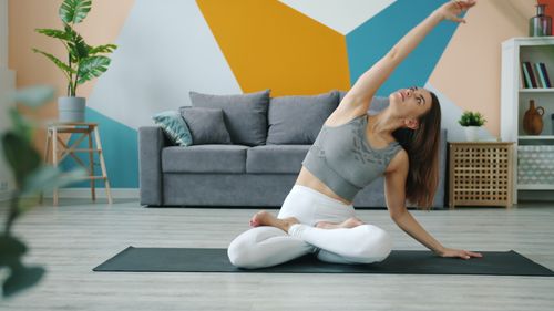 Free Woman in activewear doing yoga in a modern living room with geometric wall design. Stock Photo